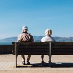 man and woman sitting on bench facing sea