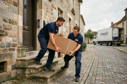 Deux déménageurs professionnels portant un carton devant une maison en pierre dans l'Aisne