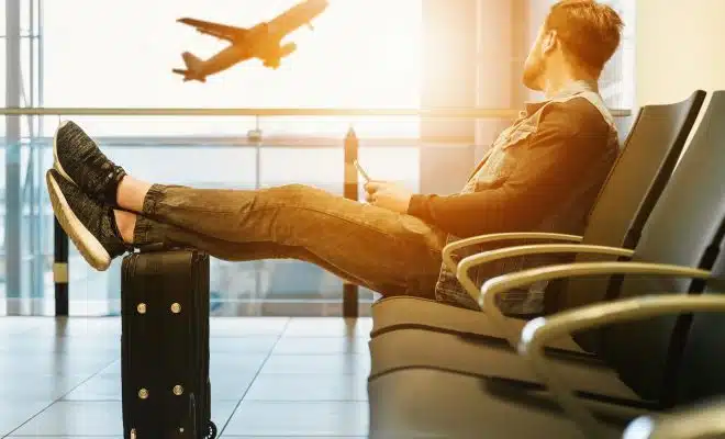 man sitting on gang chair with feet on luggage looking at airplane